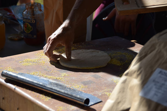A person shaping pizza dough on a wooden board dusted with cornmeal